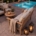 Teakhouten loungeset met gevlochten wicker zijpanelen en beige kussens op een terras bij een zwembad