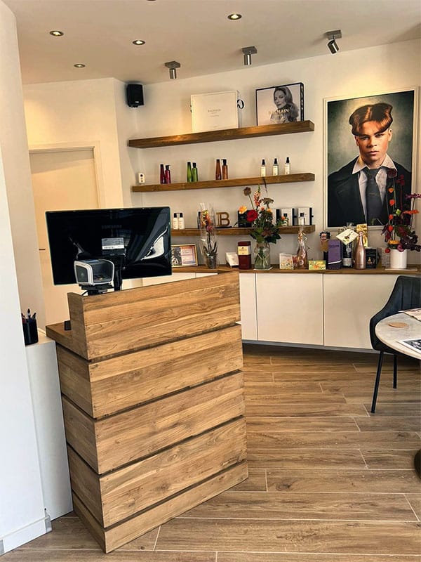 Teakhouten receptiebalie en wandplanken in de inrichting van een moderne kapperszaak